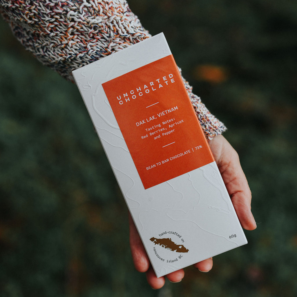 A hand holding a bar of Uncharted Chocolate 73% Dak Lam Vietnam single origin chocolate.